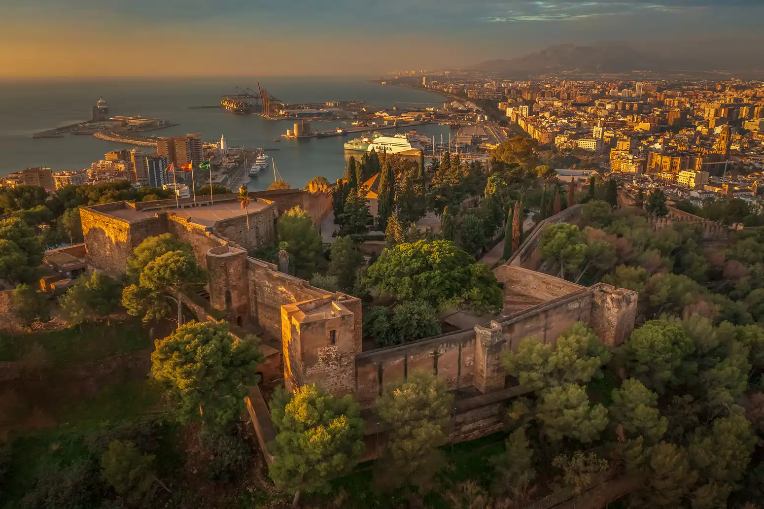 Mauern der Alcazaba von Málaga bei Sonnenuntergang, mit dem Hafen im Hintergrund