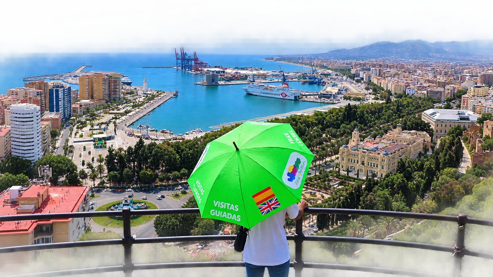 Luftaufnahme des Hafens und der Bucht von Málaga mit einer Person mit grünem „Stadtführungen“-Regenschirm im Vordergrund
