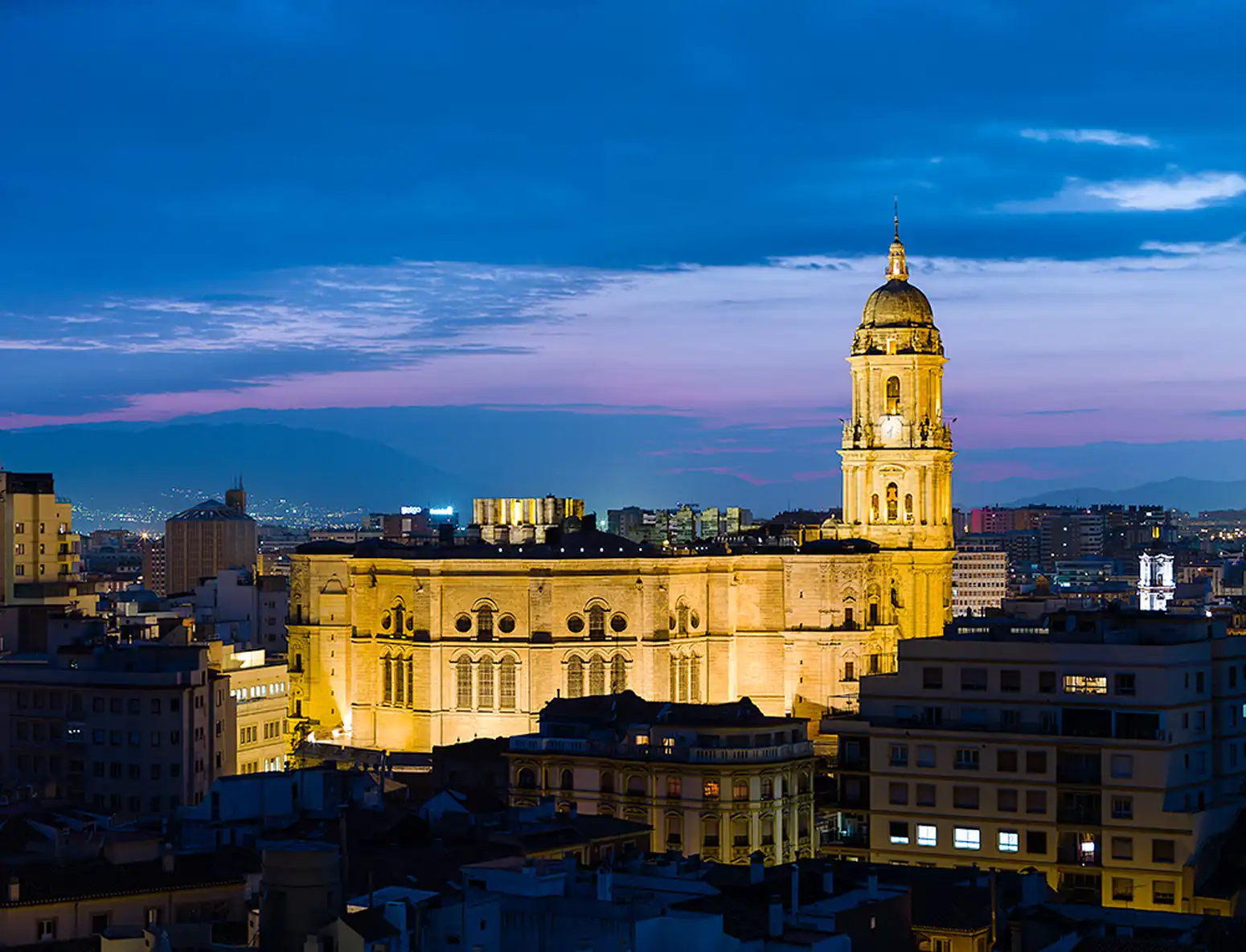 La cathédrale de Málaga illuminée à la tombée de la nuit au-dessus des toits du centre